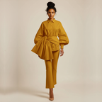 Woman wearing a mustard yellow outfit with a tied waist on a beige background