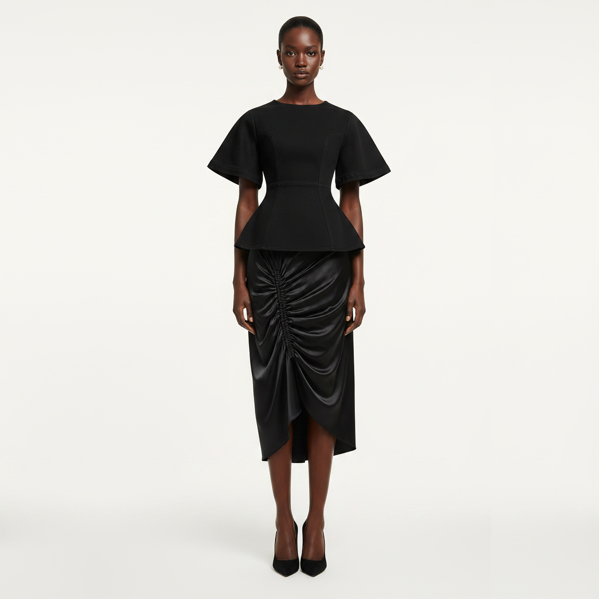 Black peplum top and ruched skirt worn by a model on a white background