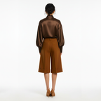 Person wearing a brown satin blouse and brown pants on a white background