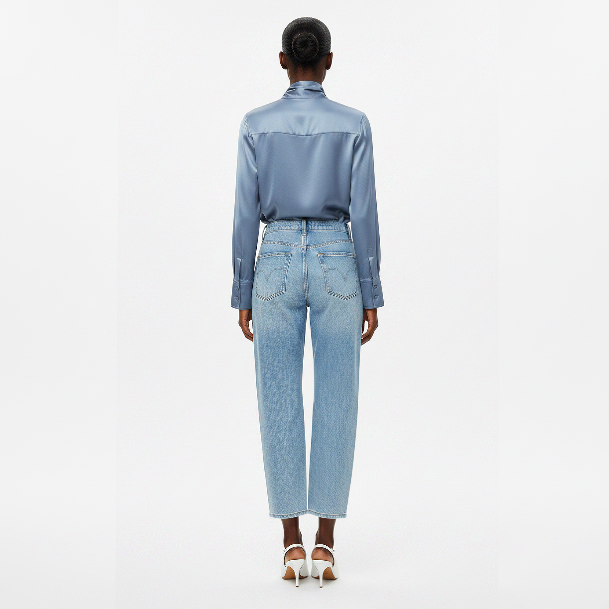 Person wearing a light blue satin shirt and jeans on a white background