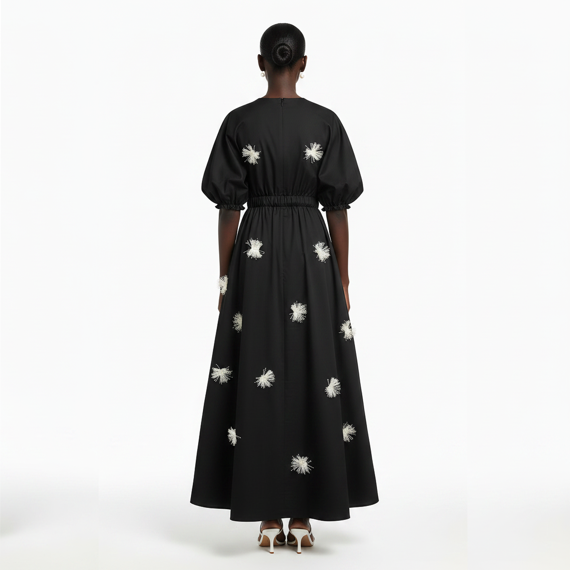 Black dress with white floral patterns worn by a model on a white background