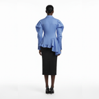 Person wearing a blue blouse with ruffled details and a black skirt on a white background