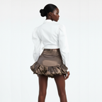 Woman wearing a white blouse and brown pleated skirt on a plain background