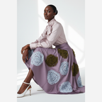 Woman wearing a light purple blouse and a long skirt with floral patterns on a white background