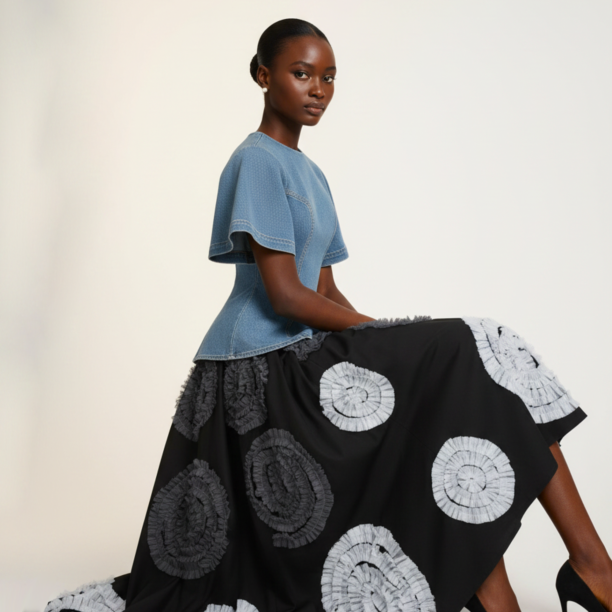 Model wearing a blue top and black skirt with white circular patterns on a plain background