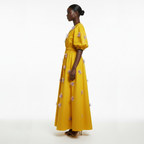 Woman wearing a yellow dress with floral details on a white background