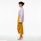 Woman wearing a light purple top and yellow skirt on a white background
