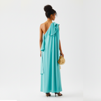 Woman wearing a turquoise one-shoulder dress holding a gold handbag on a white background