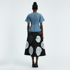 Woman wearing a denim top and black skirt with white patterns on a white background