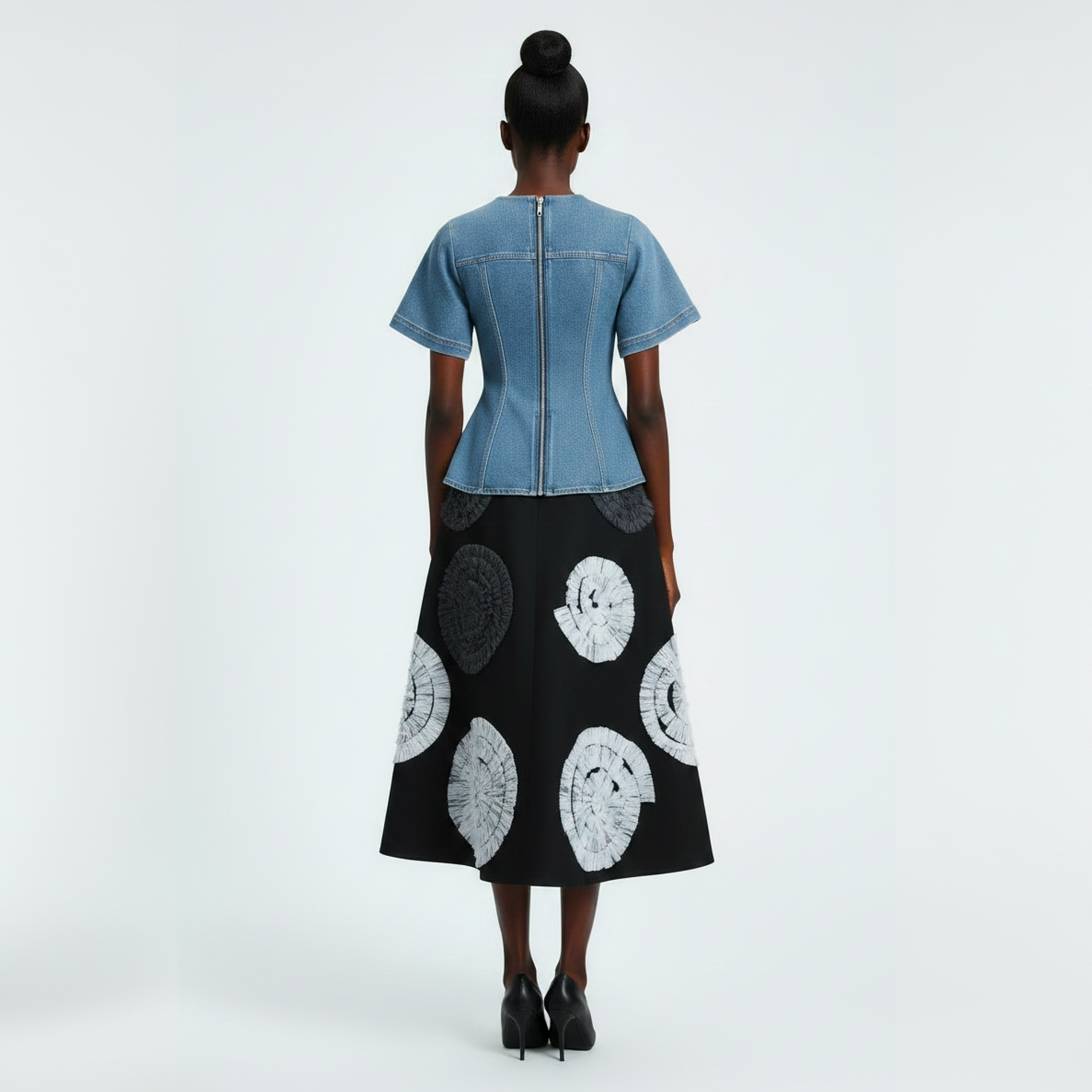Woman wearing a denim top and black skirt with white patterns on a white background