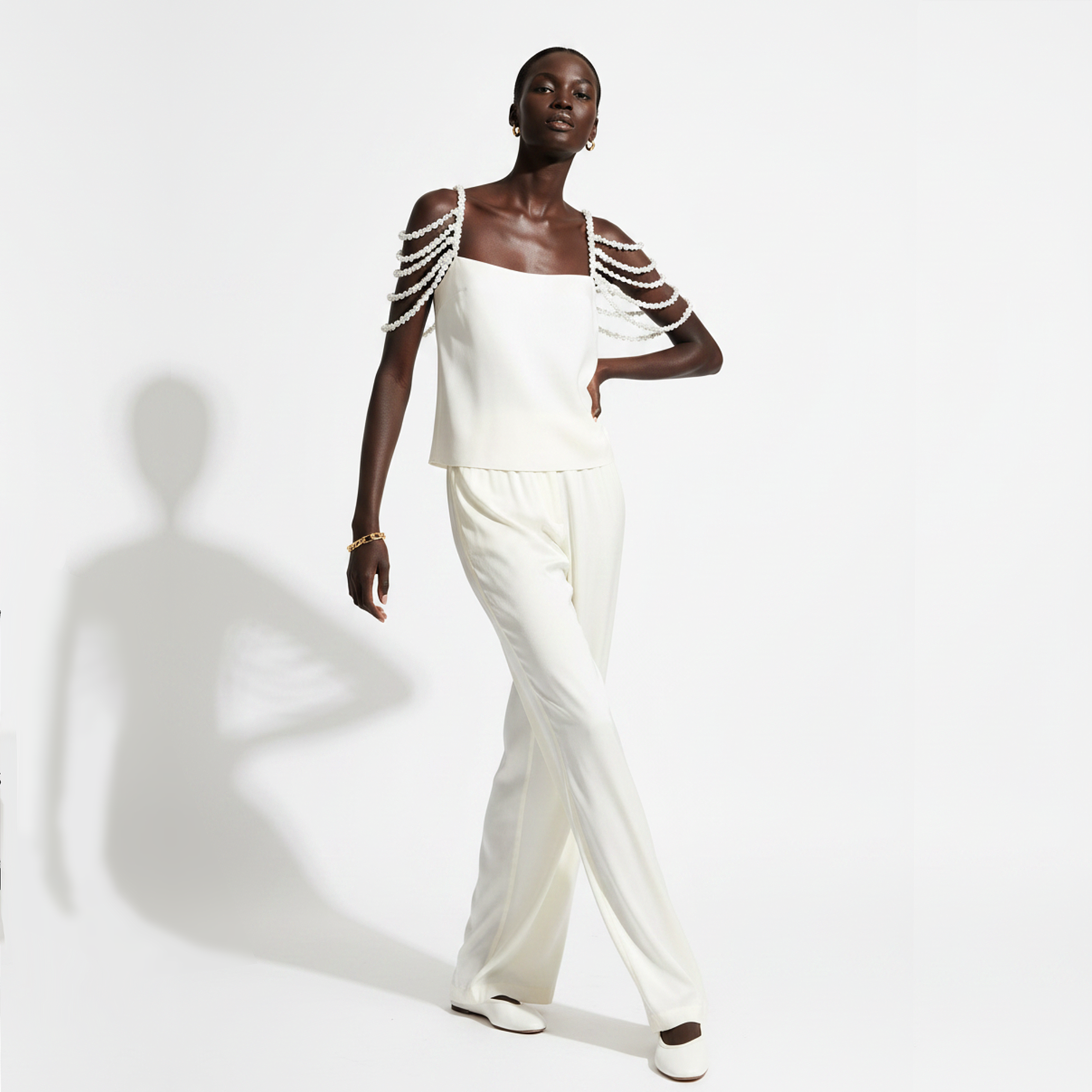 A person wearing a white top with pearl shoulder straps on a white background