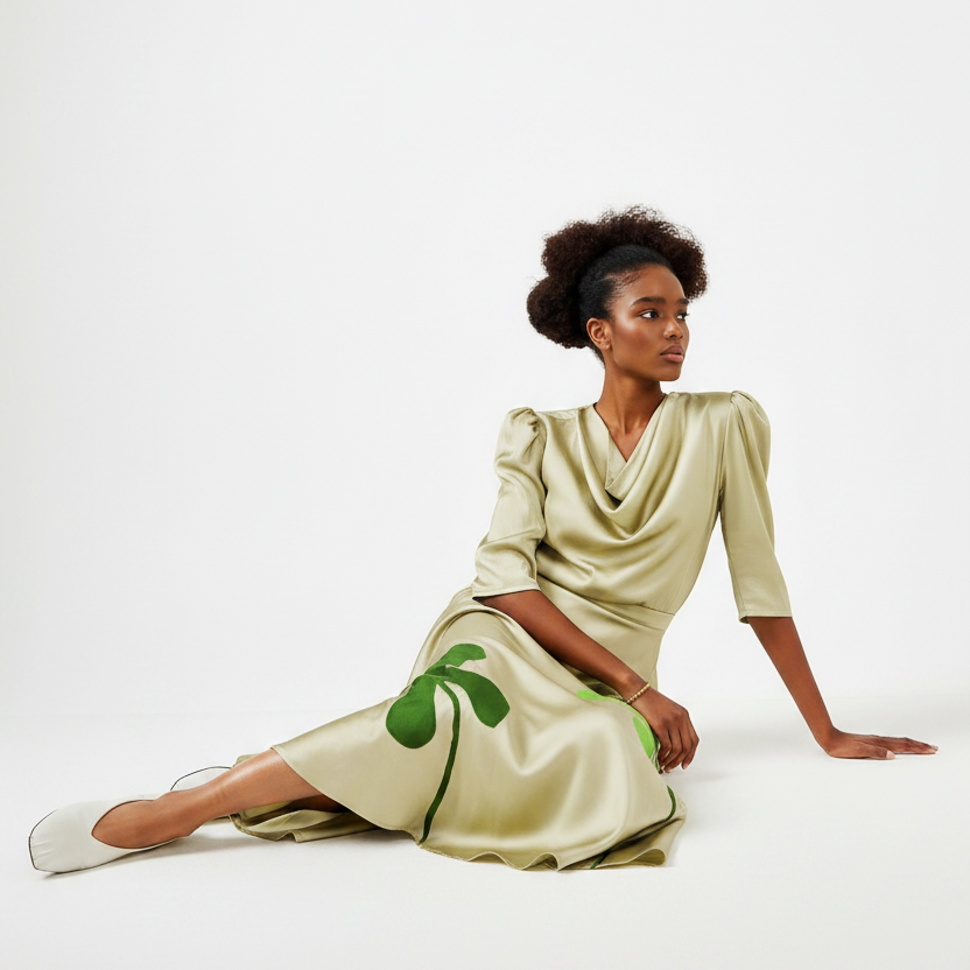Woman wearing a beige dress with green clover patterns on a white background