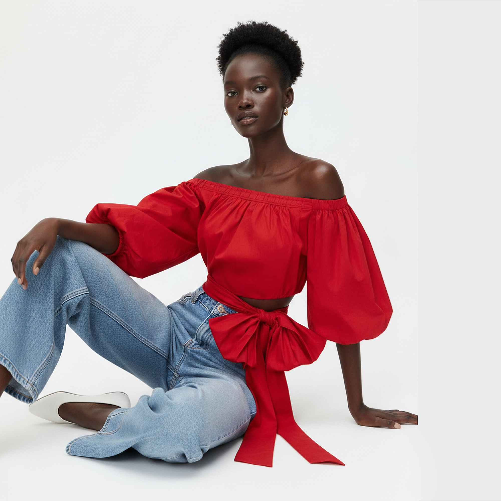Woman wearing a red off-shoulder top with a blue jeans on a white background